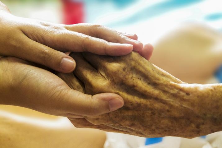 A younger hand holds an elderly person's hand.