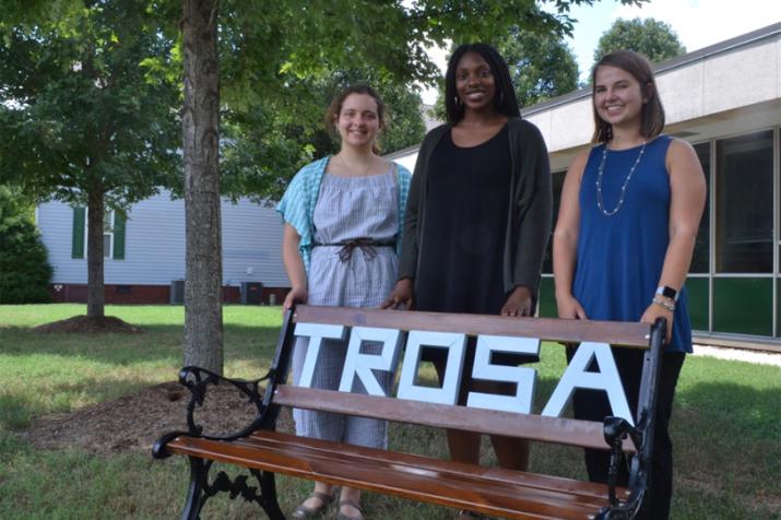 DGHI interns stand by a bench that reads "TROSA" in Durham.