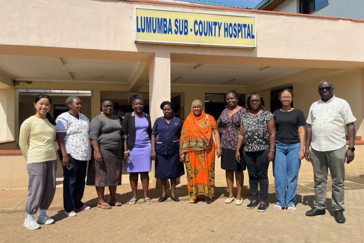 10 people stand in front of Lumumba Sub-County Hospital. Project leads Sydney Chen is to the far left and Melat Woldetensae is second from the right.